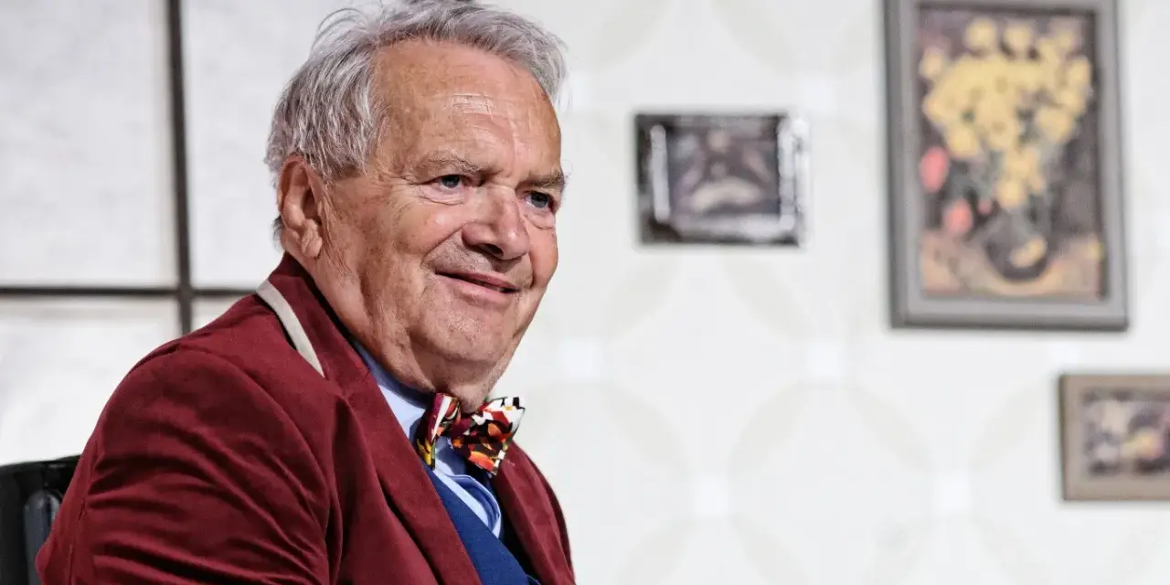 Uśmiechnięty Zdzisław Wardejn, znany z wielu filmów, w bordowym marynarkowym stroju i kolorowym krawacie.