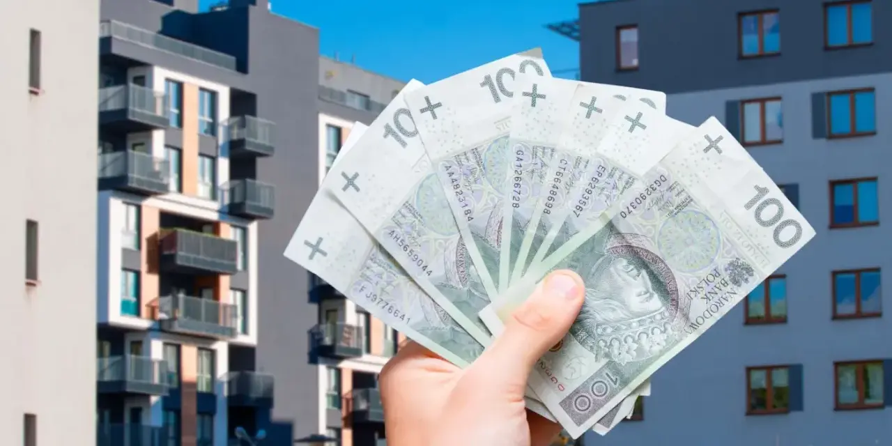 Dłoń trzyma banknoty 100 zł na tle nowoczesnych budynków mieszkalnych. Symbolizuje to podatek od sprzedaży nieruchomości.
