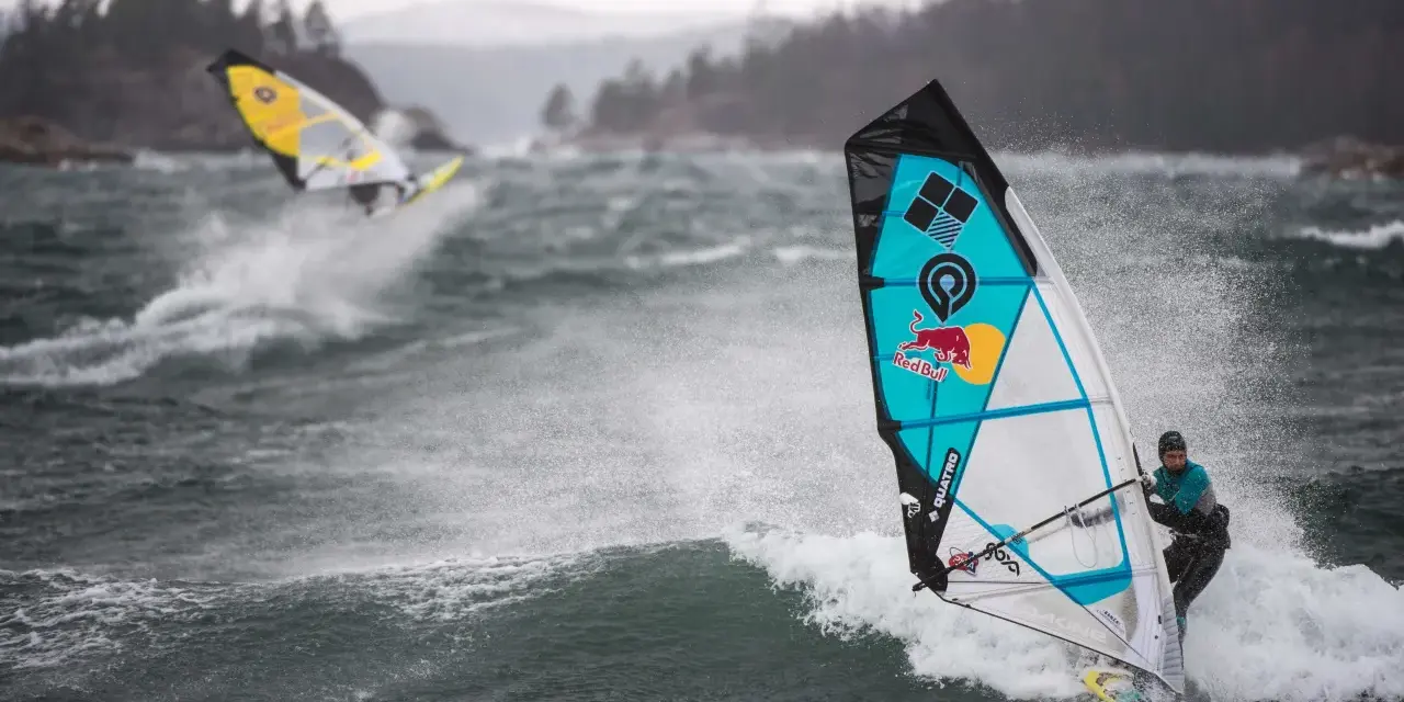 Windsurferzy na falach, jeden z nich na pierwszym planie, w akcji.
