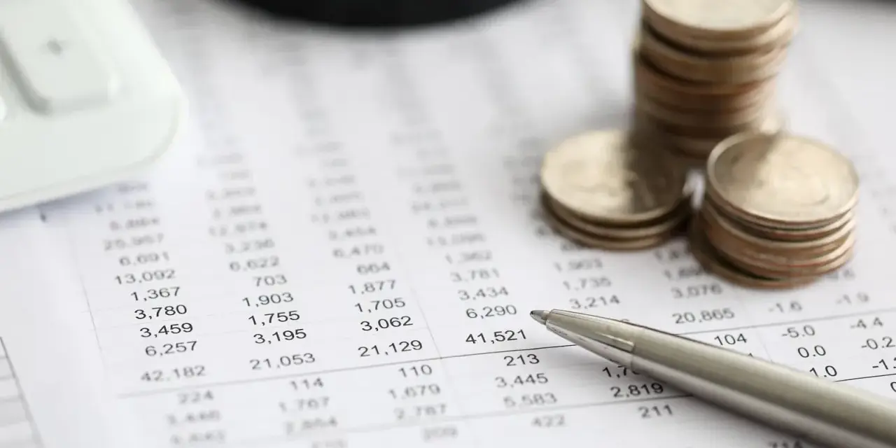 Monedas apiladas sobre un informe financiero, con una calculadora y un bolígrafo. El informe muestra números, quizás el modelo 420.
