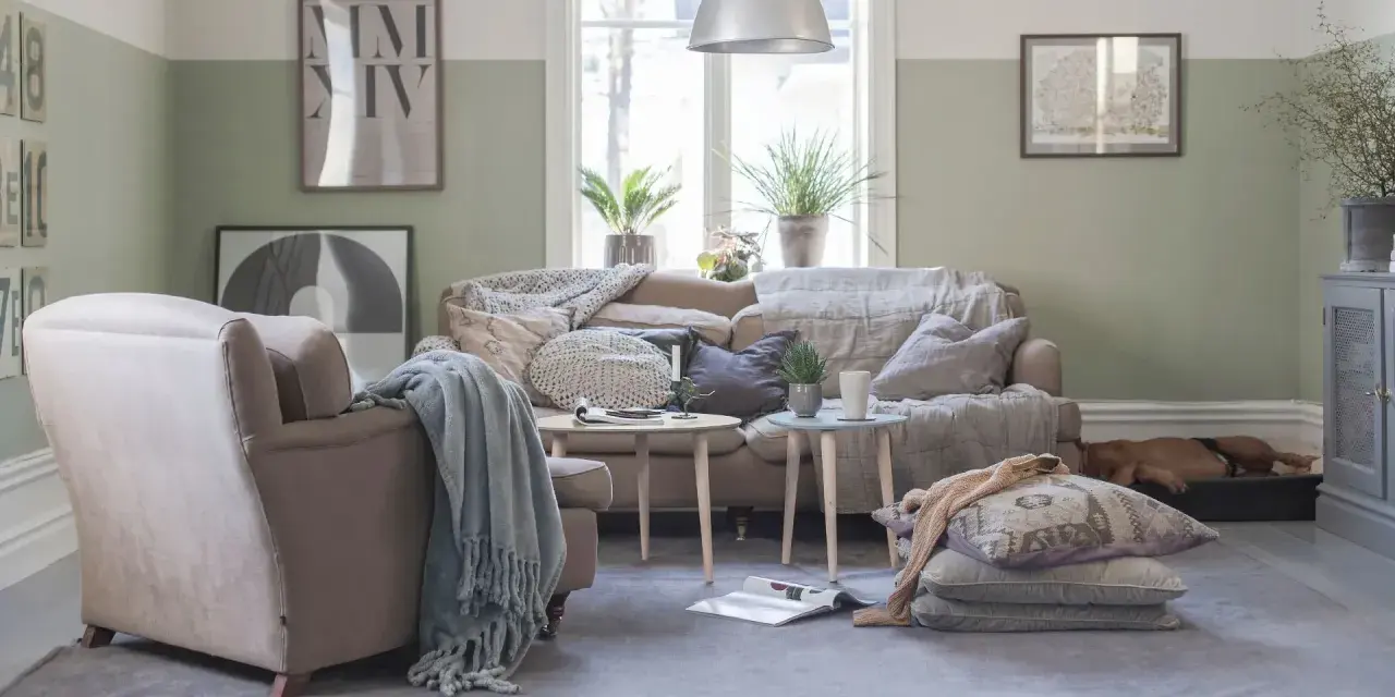Vardagsrum i svensk stil med bekväm soffa, fåtölj och en sovande hund. Vårljus strömmar in genom fönstret och skapar en mysig atmosfär.