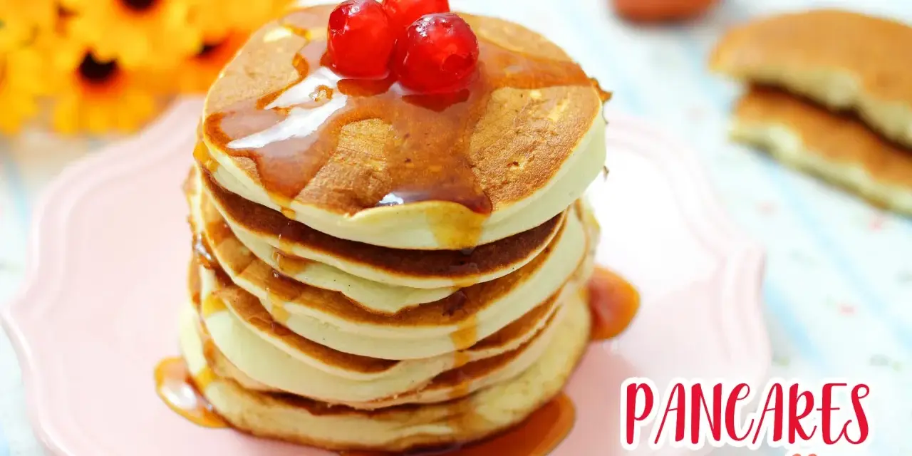 Pancakes con albumi, soffici e dorati, guarniti con sciroppo e ciliegie rosse, su un piatto rosa.