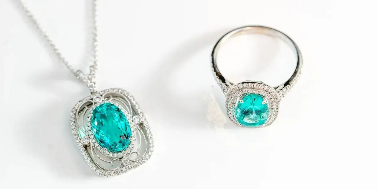 Conjunto de collar y anillo con una deslumbrante piedra de geminis turquesa rodeada de diamantes, sobre fondo blanco.