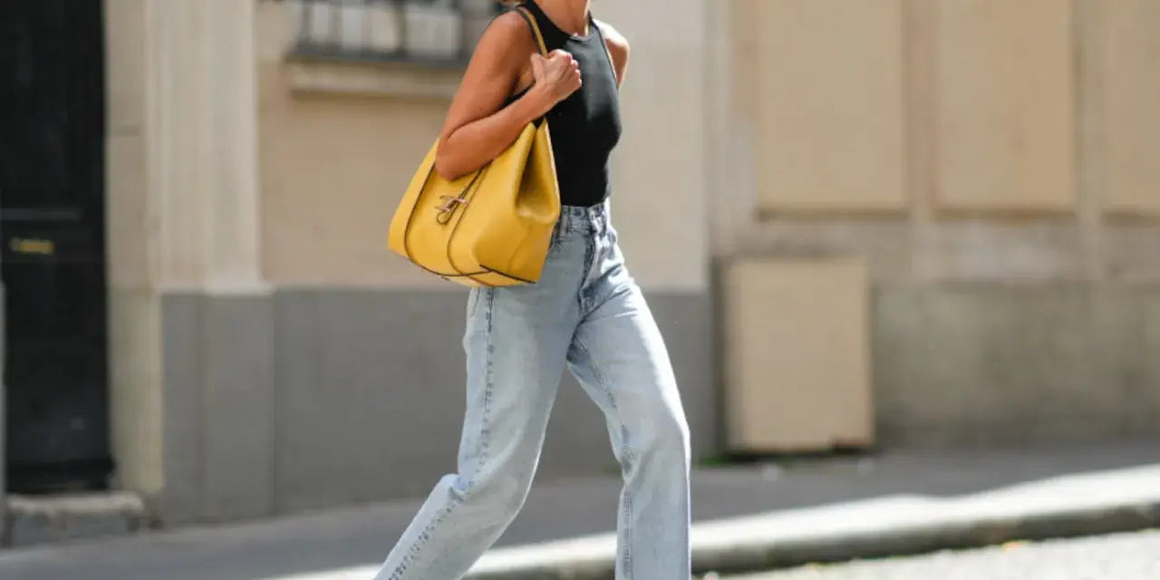 Mujer con vaqueros anchos de tiro alto, un top negro y un bolso amarillo vibrante. Un ejemplo de los diversos tipos de vaqueros mujer.