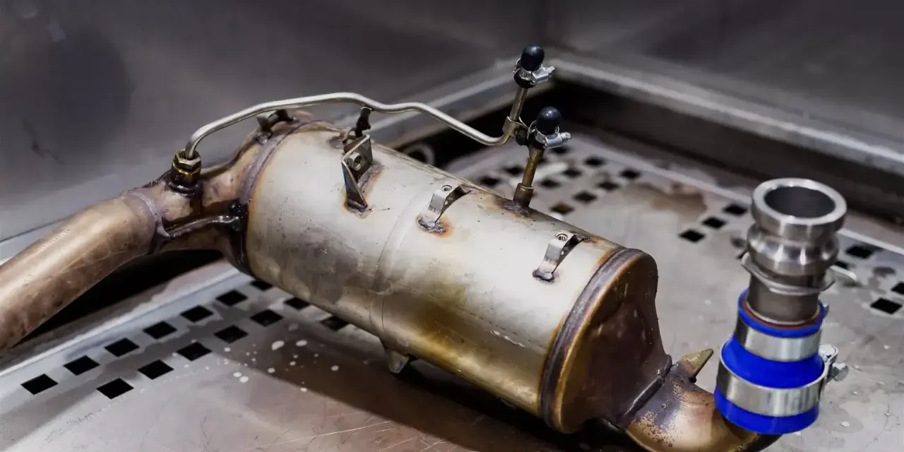 Metalowy element układu wydechowego, prawdopodobnie zapchany dpf, leży na metalowej powierzchni.