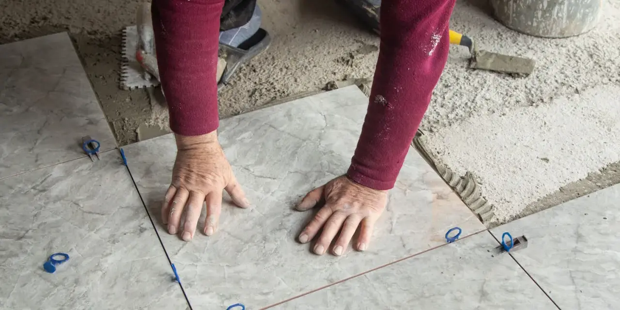 Mani esperte posano mattonelle con precisione, usando livellatori per un risultato perfetto.