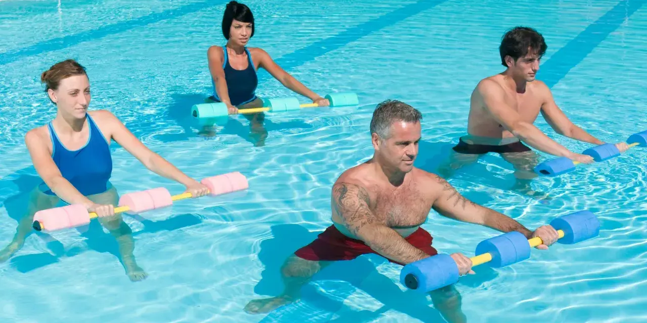 Quatre personnes font un exercice piscine avec des haltères flottants. L'eau bleue reflète la lumière du soleil.