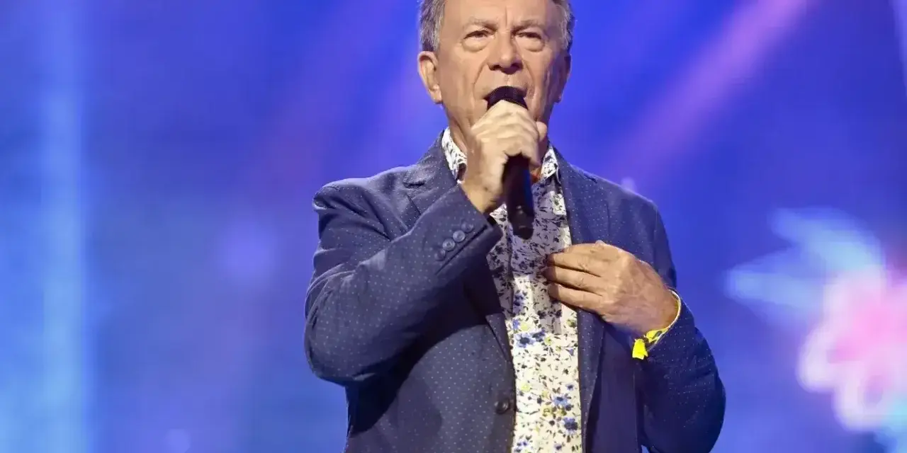Wojciech Gąsowski w niebieskiej marynarce w kropki i kwiecistej koszuli śpiewa na scenie.