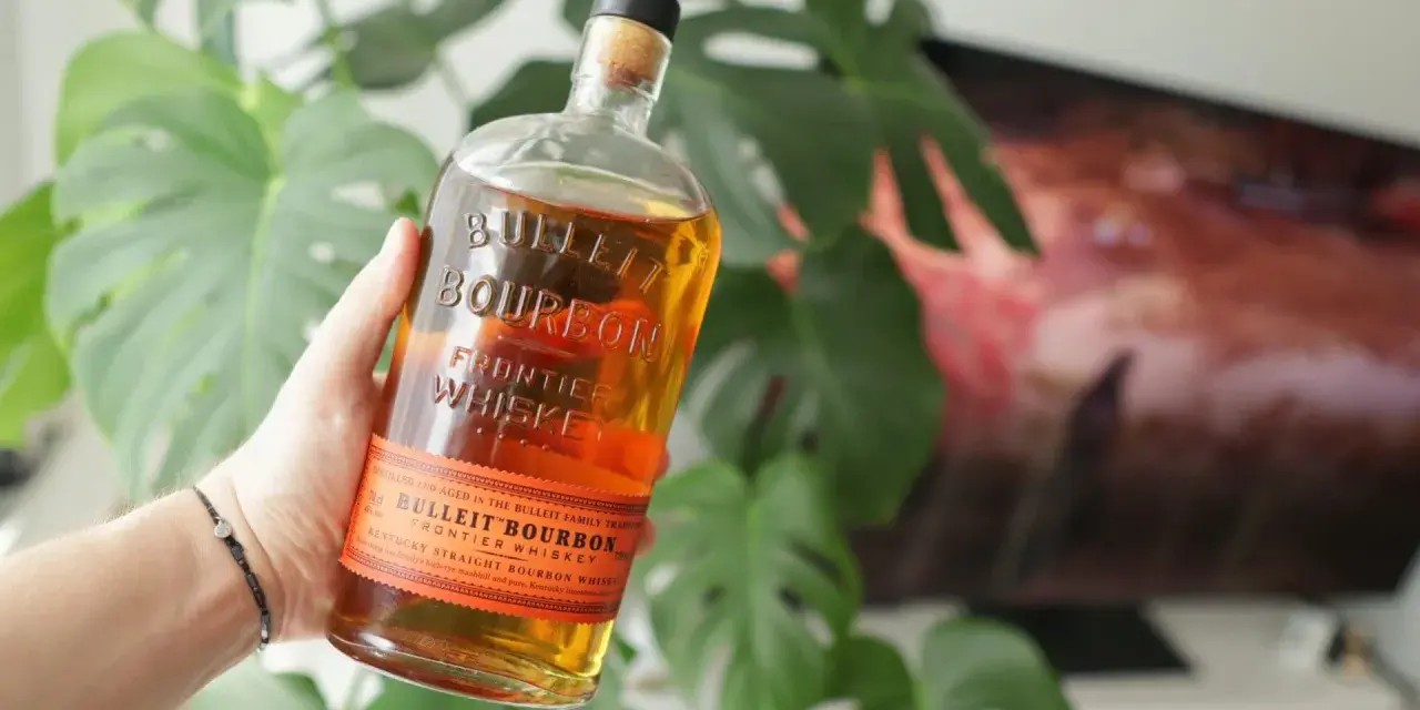 Dłoń trzyma butelkę Bulleit Bourbon. To Kentucky Straight Bourbon Whiskey, idealny do drinków.