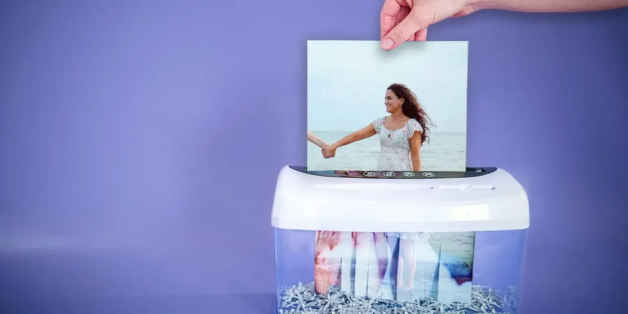 Eine Hand führt ein Foto eines Paares am Strand in einen Aktenvernichter. Was bedeutet familienstand?