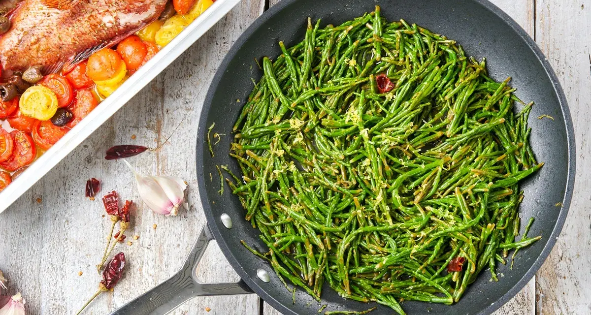 Asparagi di mare saltati in padella con aglio e peperoncino, accanto a un pesce al forno con pomodorini.