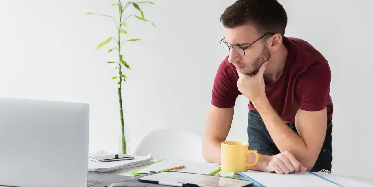 Joven autónomo reflexiona en su escritorio. Lo cotizado como autónomo cuenta para el paro, una tranquilidad para su futuro.
