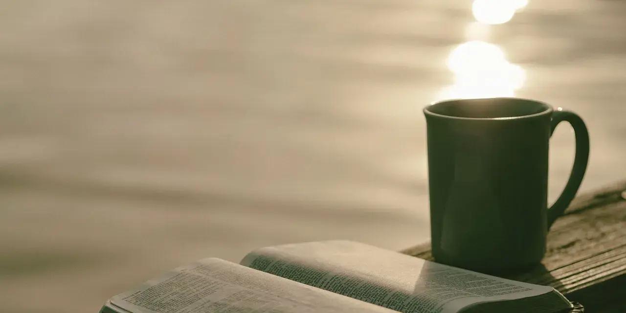 Offenes Buch mit Bibelversen, Tasse Kaffee am Seeufer. "Ich liebe den Herrn, denn er hört meine Stimme" (Psalm 116:11).
