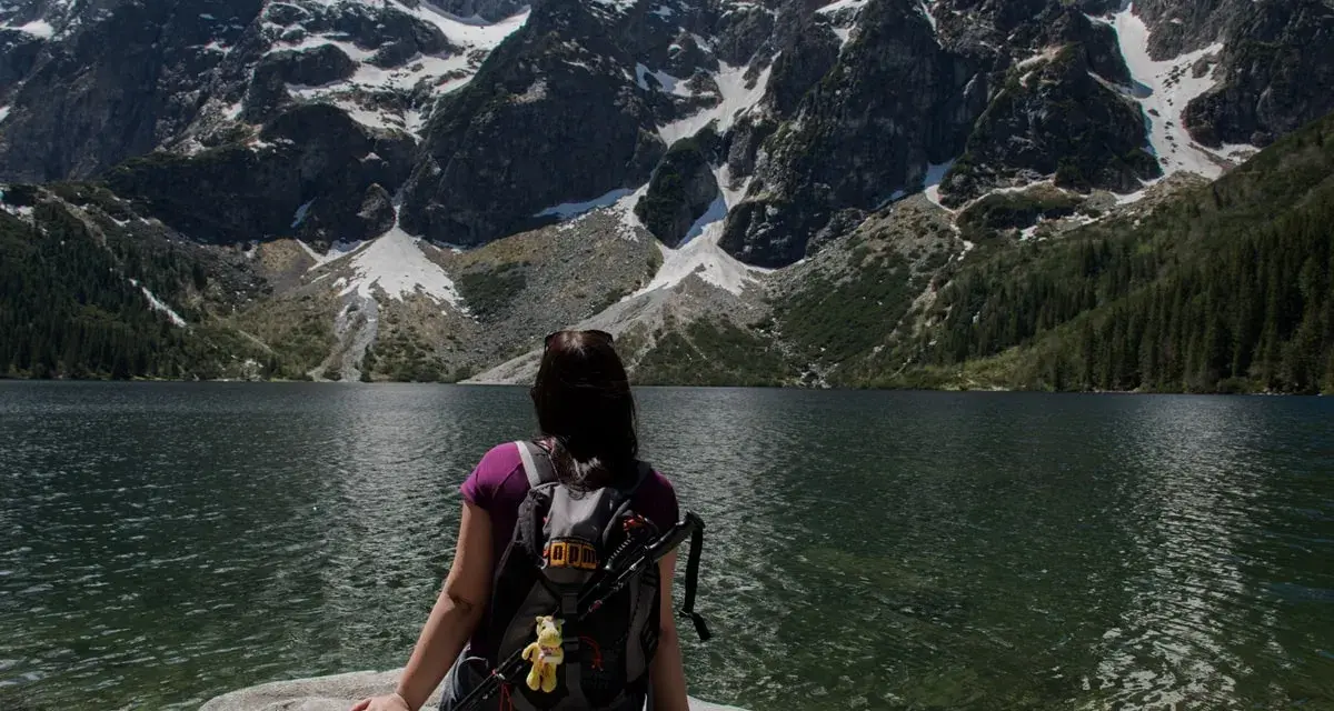 Widok na Morskie Oko z perspektywy turystki. Góry pokryte śniegiem, las i tafla jeziora tworzą malowniczą trasę.
