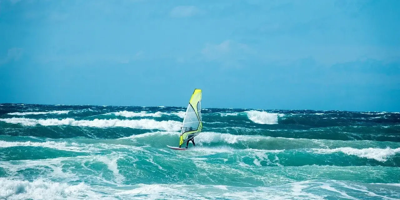 Windsurfer na wzburzonym, turkusowym morzu pod błękitnym niebem.