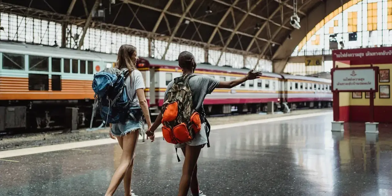 Dwie podróżniczki z plecakami idą wzdłuż peronu, gdzie stoi długi pociąg. Może to być ich pierwszy pociąg Eurostar.
