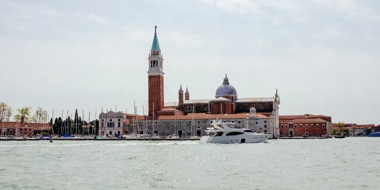 Un'isola di Venezia nascosta, con un campanile imponente, una chiesa con cupola e uno yacht che solca le acque.