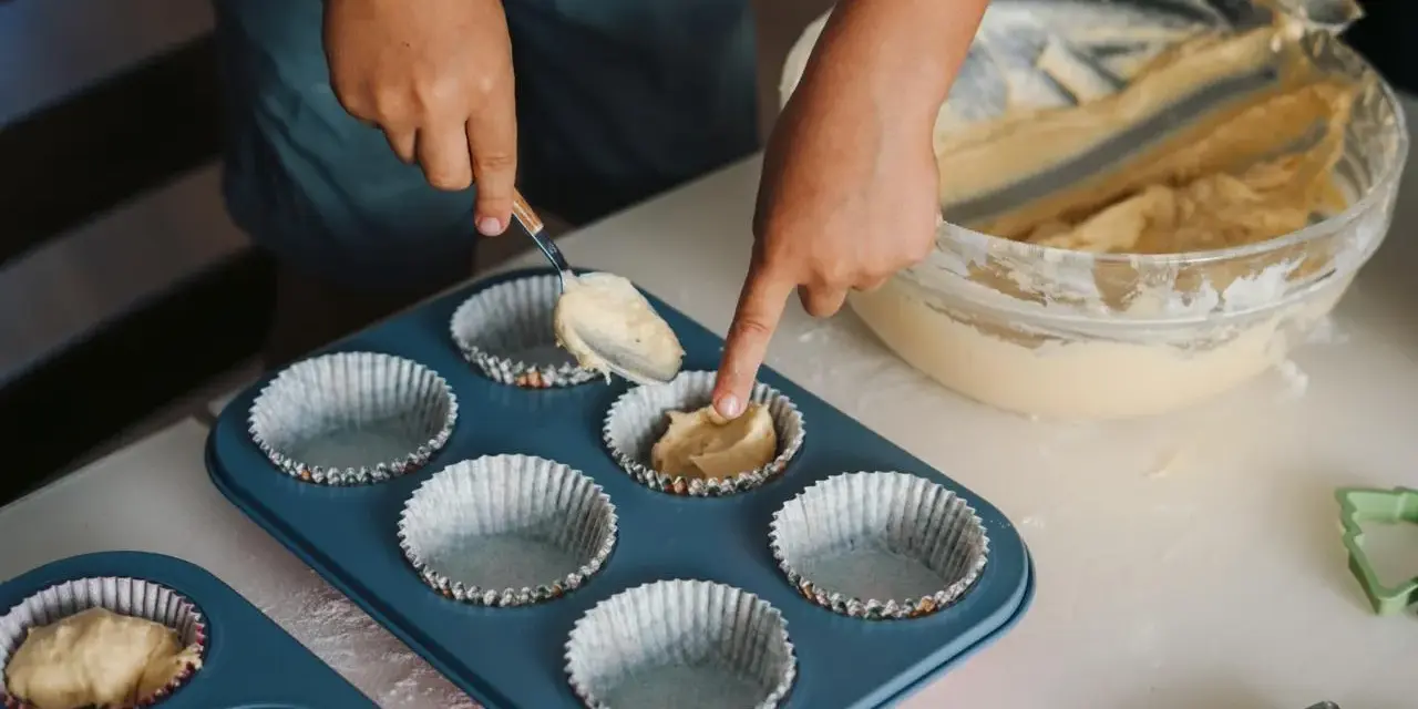 Dziecko nakłada ciasto na muffinki łyżką do formy.