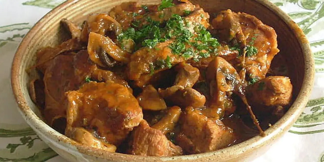 Un délicieux sauté de veau aux champignons, garni de persil frais, servi dans un bol en terre cuite.
