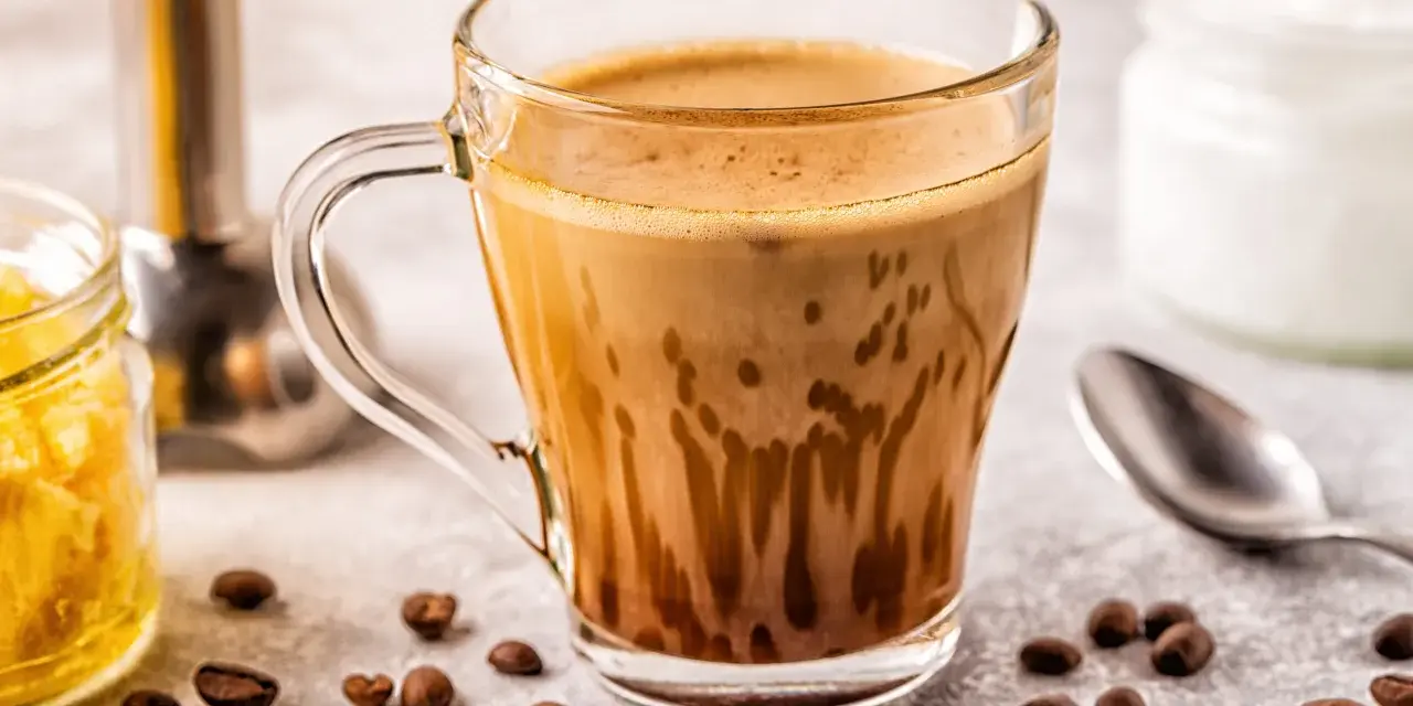 Kawa bullet coffee w szklance, obok ziarna kawy, słoiczek z miodem i łyżeczka.