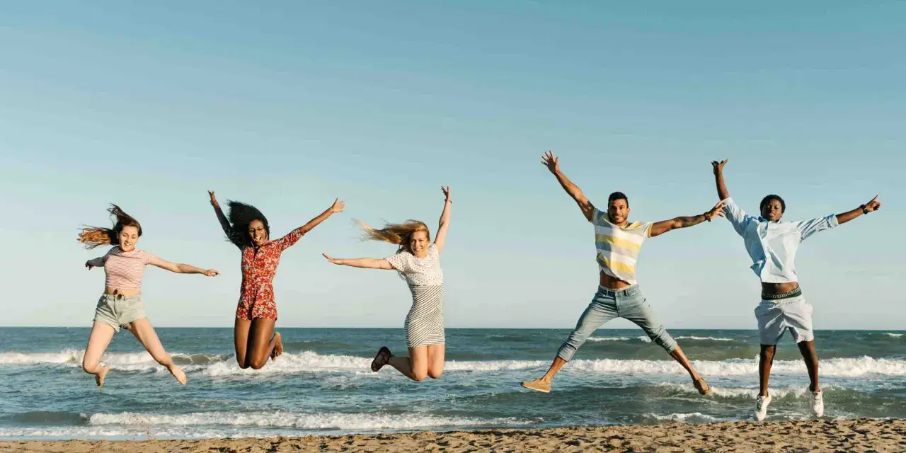 Fünf junge Leute springen ausgelassen am Strand. Sie freuen sich über ihr Sprachreise Stipendium und die Freiheit.