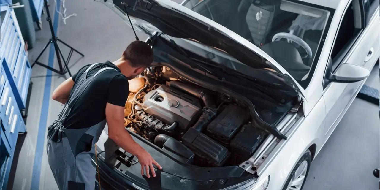 Młody mechanik w kombinezonie pracuje przy silniku białego samochodu. To jego pasja, każdy konstruktor marzy o takiej precyzji.