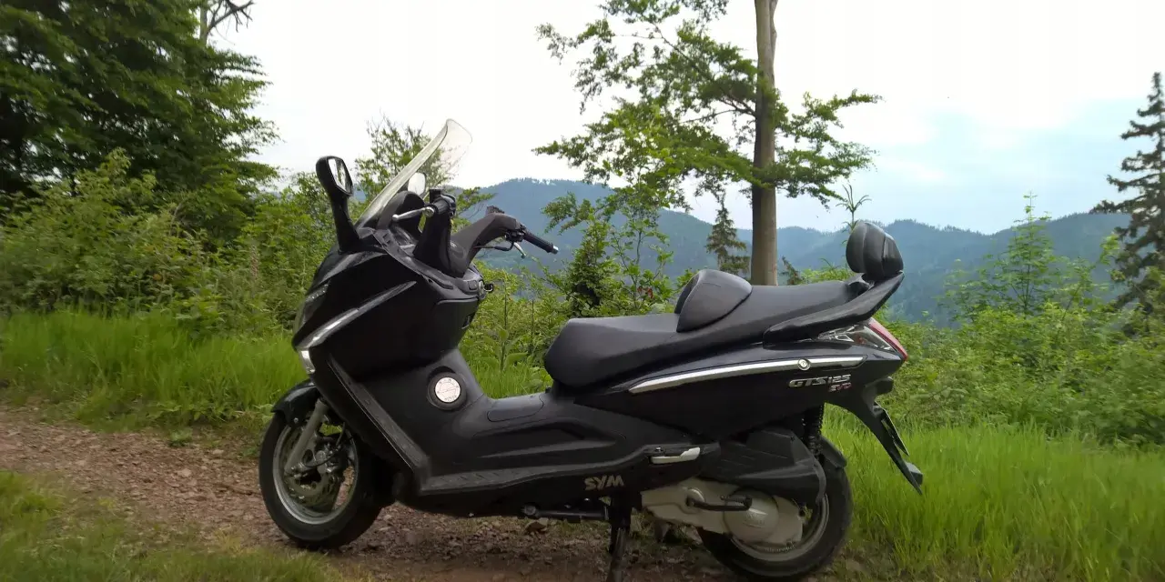 Czarny skuter Sym GTS 125 na górskiej drodze. Jego prędkość maksymalna pozwala na odkrywanie malowniczych zakątków.