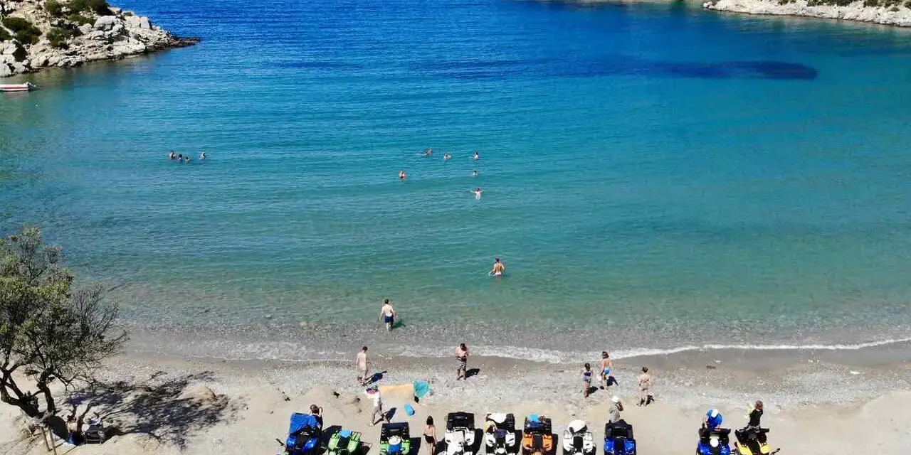 Linia pojazdów terenowych na plaży w Poros, Grecja, czeka na chętnych do zwiedzania. W tle turkusowe morze i skaliste wybrzeże.