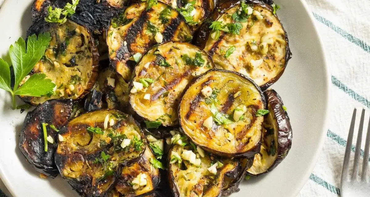 Rodajas de berenjenas a la plancha, doradas y tiernas, con ajo picado y perejil fresco. Un plato sencillo y delicioso.