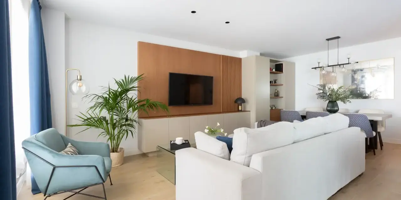 Un elegante salón moderno blanco con sofá, sillón azul, planta y mesa de comedor.