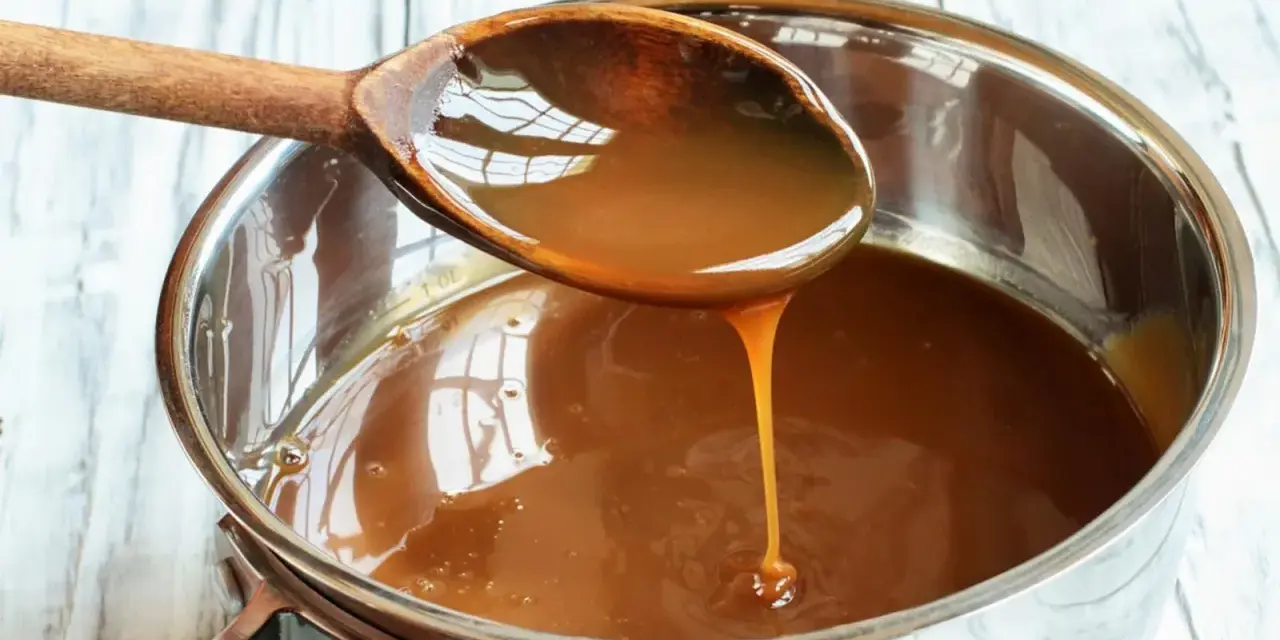 Caramelo líquido cayendo de una cuchara de madera a una olla, perfecto para tu flan al estilo Eva Arguiñano.