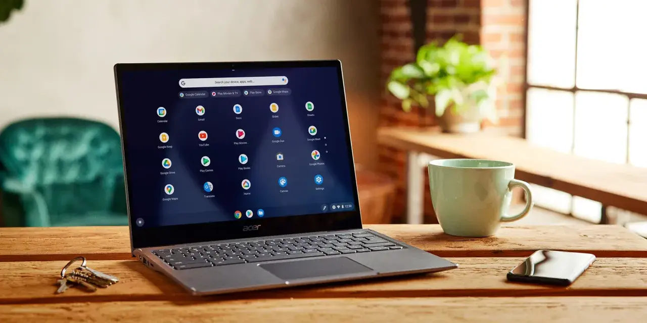 Laptop z systemem Chrome OS Flex, gotowy do pobrania, na drewnianym stole obok kubka i kluczy.