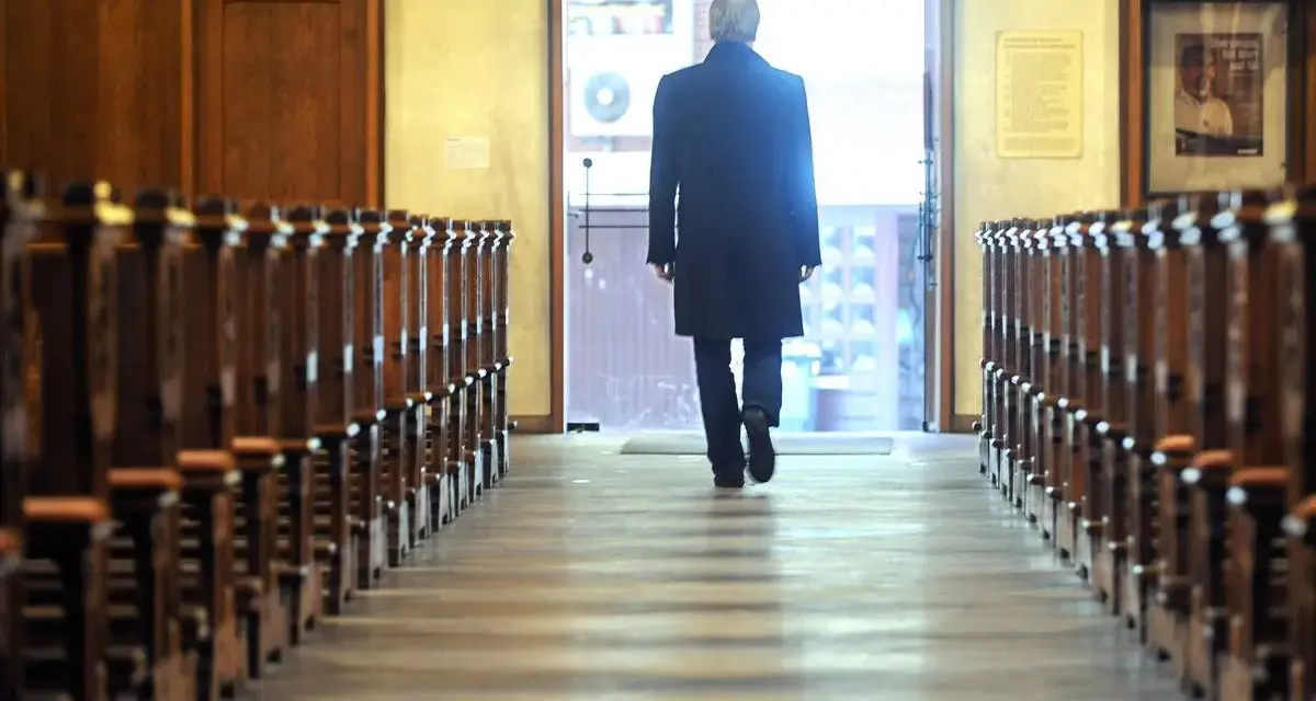 Mann verlässt Kirche in NRW. Er geht durch den Gang zwischen den Kirchenbänken zum Ausgang.