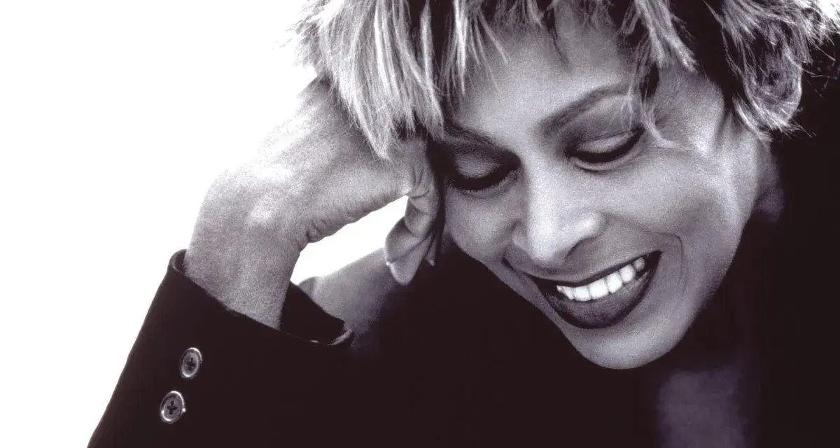 Tina Turner lächelt mit geschlossenen Augen, die Hand am Kopf. Ein ikonisches Bild der Musiklegende.