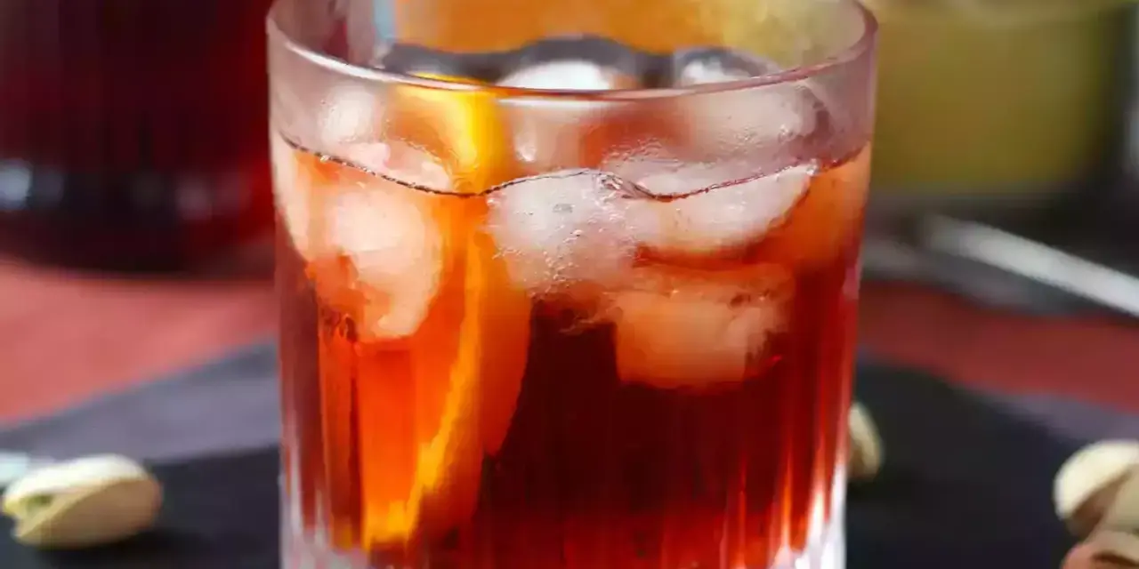 Szklanka z czerwonym drinkiem, lodem i plasterkiem pomarańczy.