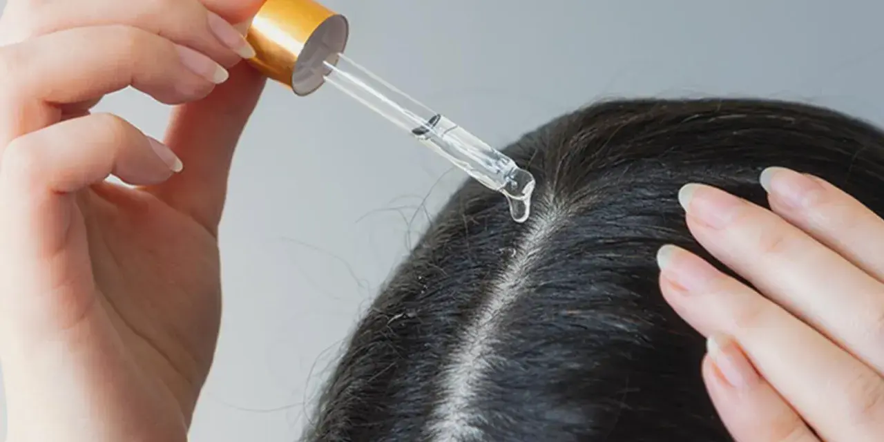 Eine Hand trägt mit Pipette ein Serum auf die Kopfhaut auf, um trockene Schuppen loswerden.