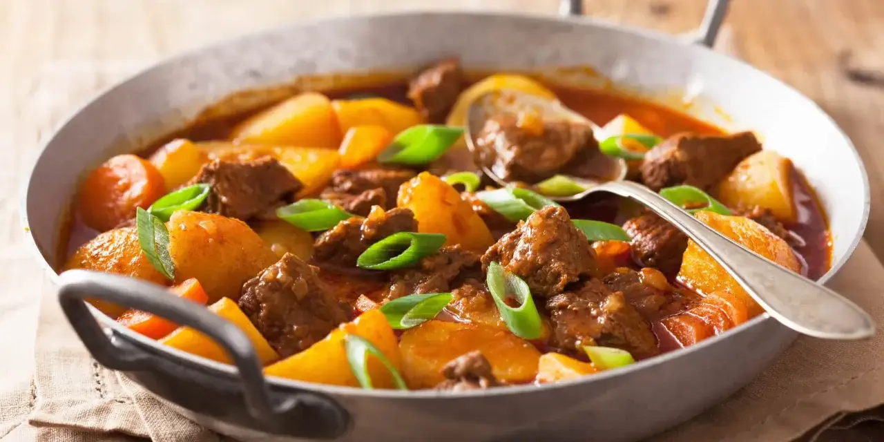 Estofado de ternera tierno con patatas y zanahorias en una sartén, adornado con cebolleta.