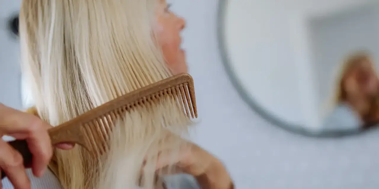 Kobieta czesze blond włosy, szukając rozwiązań co na wypadanie włosów po ciąży.