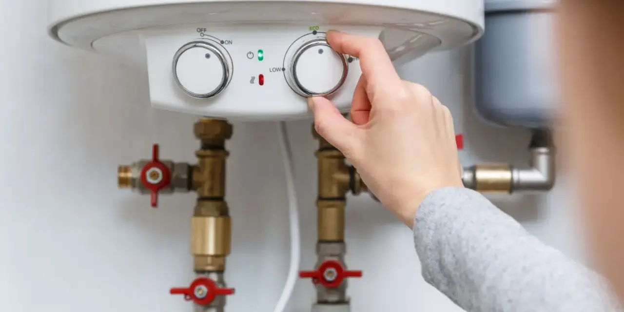 Adjusting the temperature dial on a water heater, showing its plumbing connections.