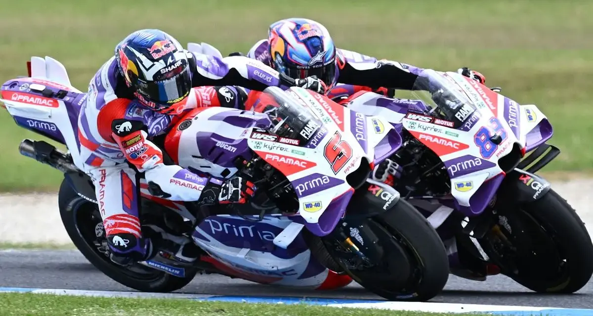 Dos pilotos de MotoGP compiten en una carrera emocionante. El piloto número 6, con casco rojo y blanco, lidera, seguido de cerca por el número 88.