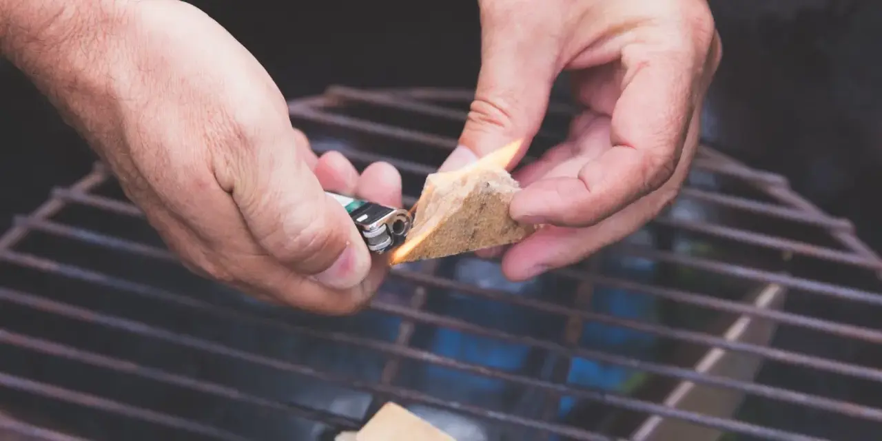 Hände zünden Grillanzünder an, um den Grill anzufeuern.