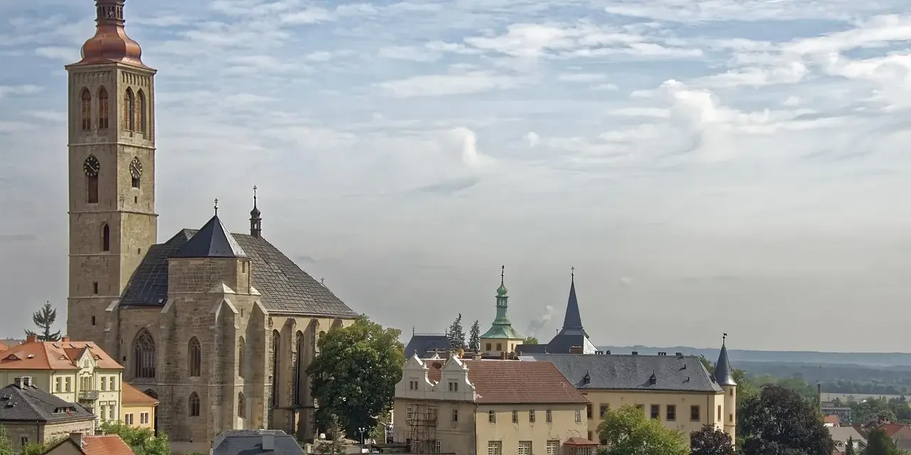 Majestatyczna katedra i zabytkowe budynki w Kutnej Horze pod błękitnym, chmurnym niebem.