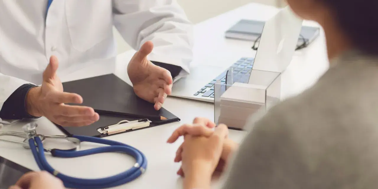 Lekarz omawia z pacjentem diagnozę, być może f43 kod choroby. Na stole stetoskop i laptop.