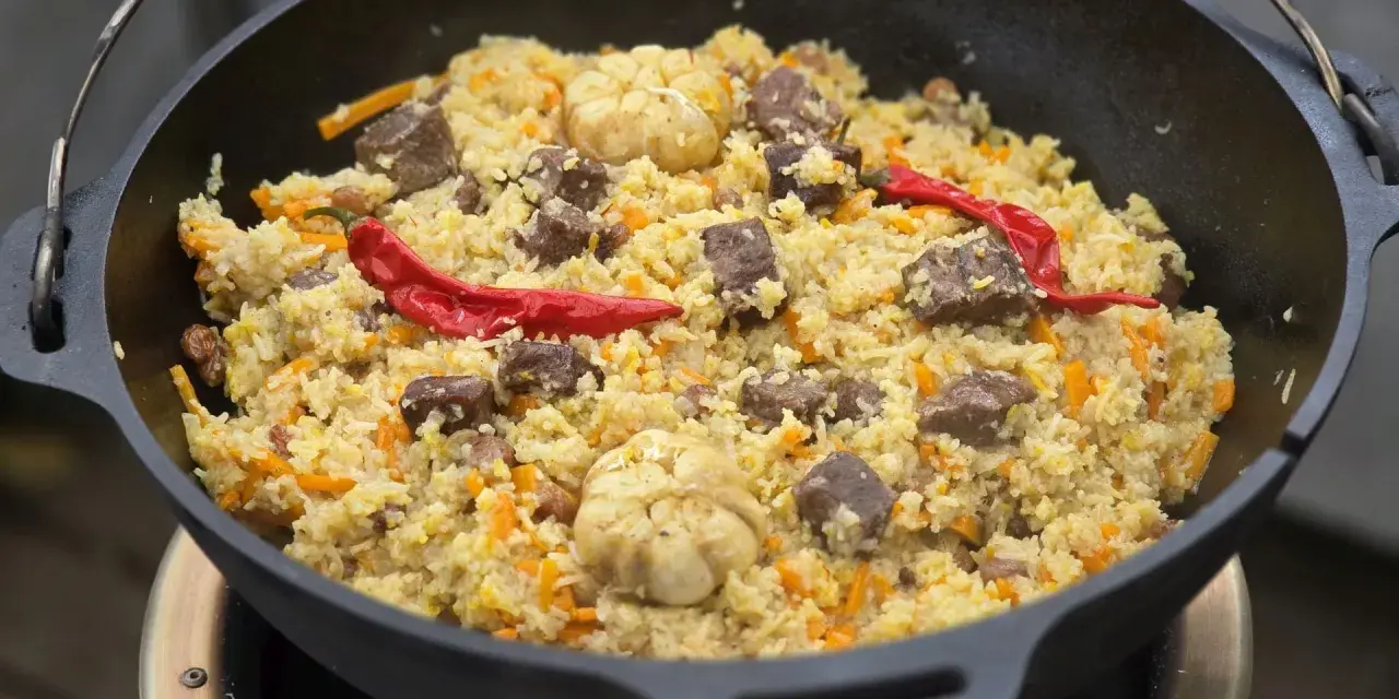 Herzhaftes Plov-Rezept im Kessel: Reis, Fleisch, Karotten, Knoblauch und scharfe Chilis. Ein Festmahl!