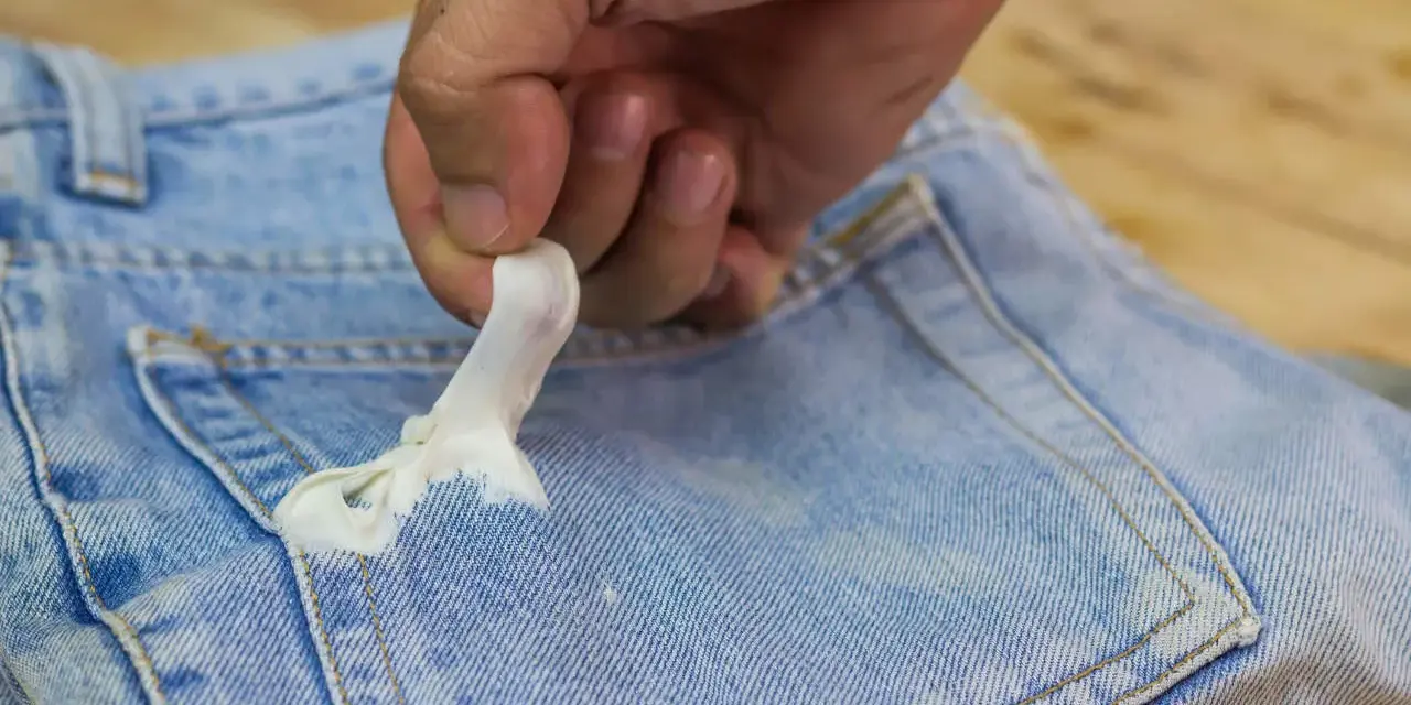 Mano quitando chicle pegado en bolsillo de jeans. Aprende como quitar chicle de la ropa fácilmente.