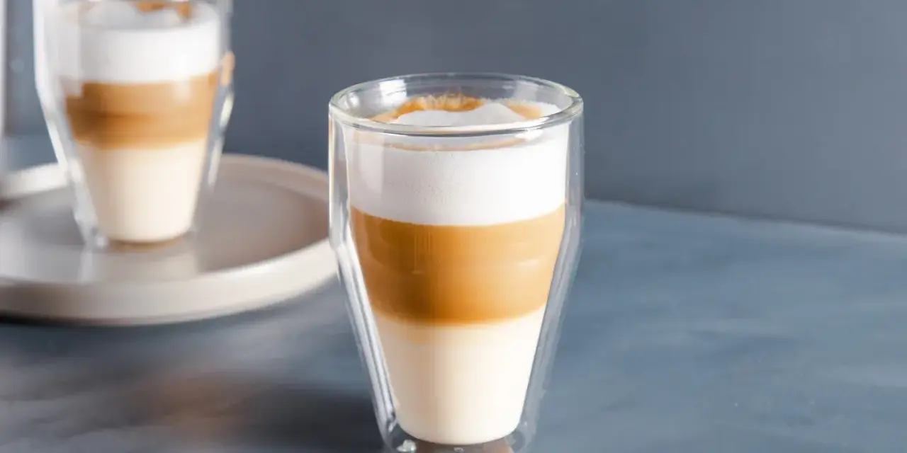 Dwa latte macchiato w szklankach z podwójnymi ściankami, z wyraźnie widocznymi warstwami mleka i kawy.