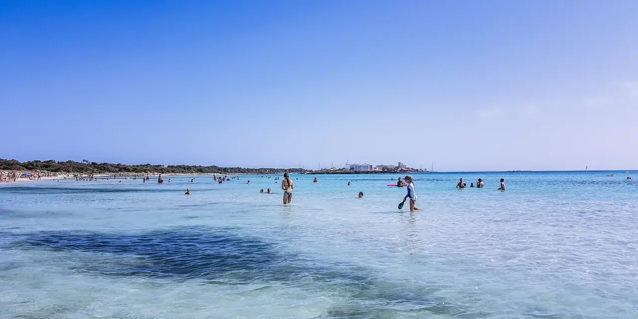 Słoneczny dzień na plaży Es Trenc. Ludzie kąpią się w krystalicznie czystej wodzie, ciesząc się wakacjami.