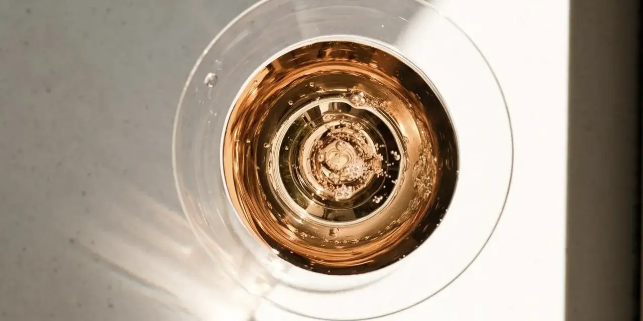 Szklanka z różowym, musującym winem, które wygląda jak tanie wino, ale jest podane w elegancki sposób. Bąbelki unoszą się ku górze.