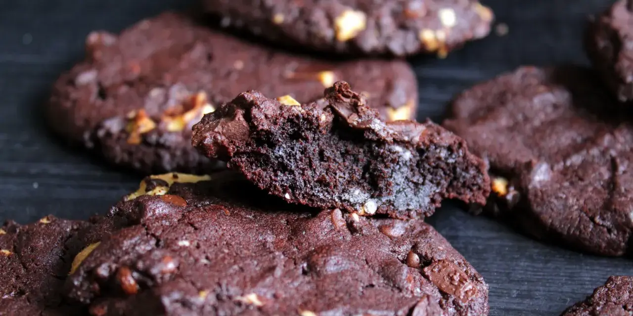 Schokoladenkekse mit Nüssen, die an das subway cookies rezept erinnern. Ein Keks ist zerbrochen und zeigt die saftige Innenseite.