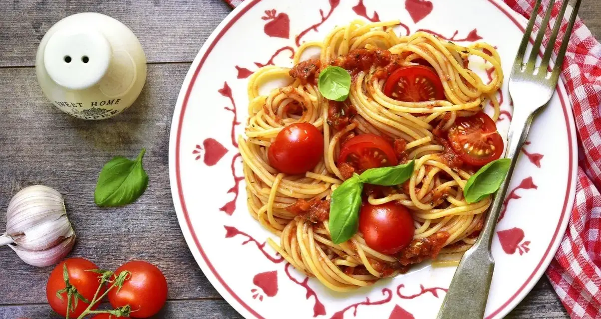 Makaron spaghetti z sosem pomidorowym, pomidorkami koktajlowymi i bazylią na talerzu.